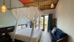 A bedroom with a bed under a canopy, a sofa, and a view of greenery outside. - Mai Chau Rustic Home - Hostel (Mai Ha)