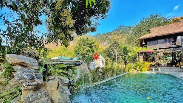 A clear pool with a waterfall feature, surrounded by lush greenery and a mountain backdrop. - Mai Chau Rustic Home - Hostel (Mai Ha)