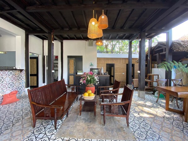 A covered outdoor seating area with wooden furniture and a tiled floor.
