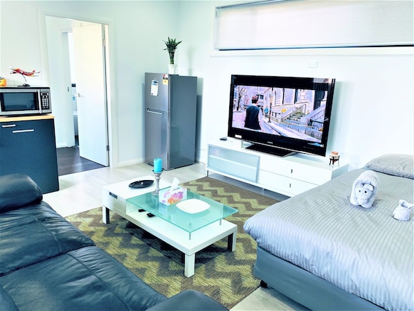A modern living room with a flat-screen TV, a sofa, a coffee table, a refrigerator, and a microwave.