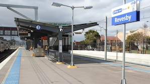 A train station platform with a shelter, a digital display, and a sign indicating 'Way out Buses'.