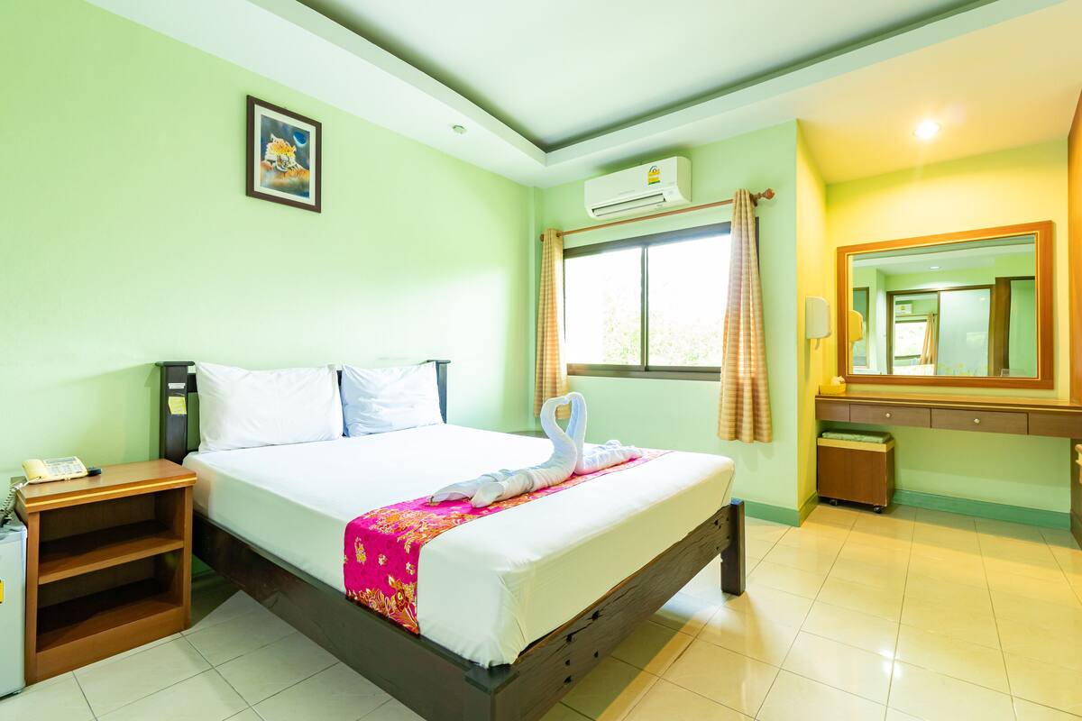 A hotel room with a bed, a nightstand, a desk, a mirror, and a window with curtains.