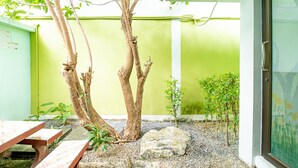 A patio area with a wooden table and benches, surrounded by a gravel ground, a small tree, and a green wall. - Khum Suk Resort (Hat Yai)