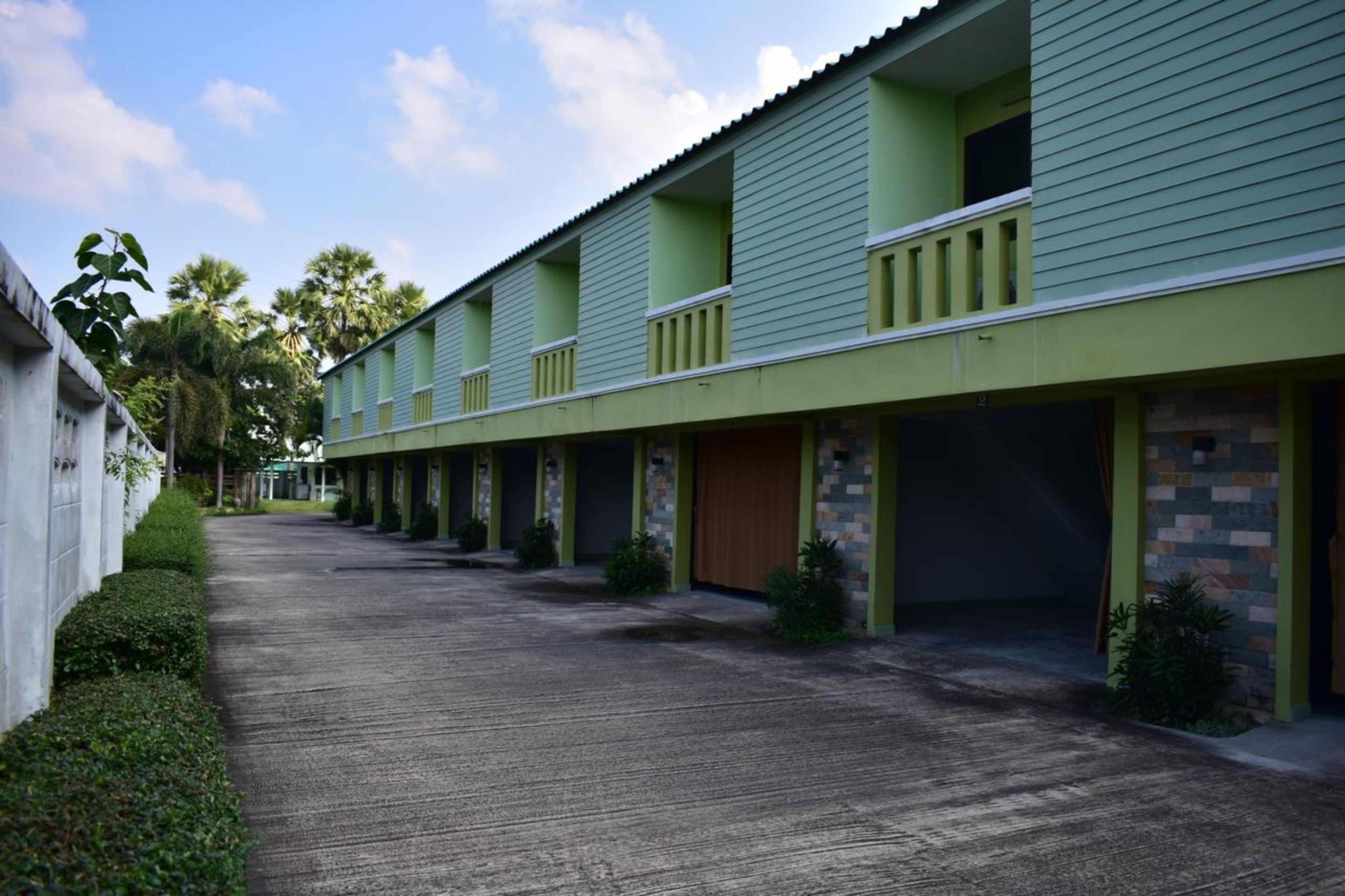 A row of green buildings with balconies, a paved walkway, and small plants.