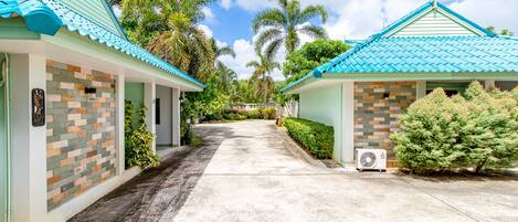A pathway leading to two buildings with blue roofs, surrounded by greenery and palm trees.