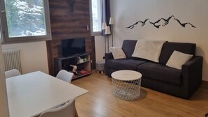 Een moderne woonkamer met een donkergrijze bank, een witte ronde salontafel en een televisie op een houten dressoir.
