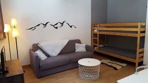 Een kamer met een grijze bank, een houten stapelbed, een rond wit bijzettafeltje en een muurstickervel met vogels.