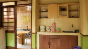 A compact kitchen with a dining area, featuring a table and chairs, a sink, and cabinets. - VILLA ADE - 0620 KOTA BUNGA PUNCAK (Cipanas)