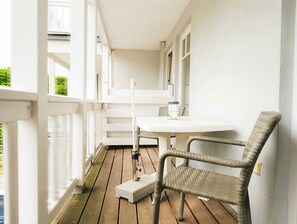 Eine Holzterrasse mit einem weißen Tisch und einem Korbstuhl.
