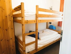 Habitación con literas, cabecero de madera, un escritorio pequeño y una silla azul.