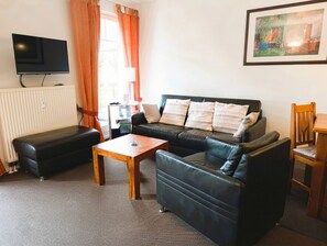 Ein Wohnzimmer mit Sofa, Hocker, Couchtisch und Fernseher.
