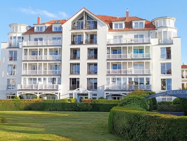 Un hotel de varios pisos con balcones, un césped cuidado y un cielo despejado.