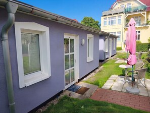 Una hilera de casas de un piso con un pequeño jardín delantero, un patio con mesa y sillas, y un paraguas rosa.