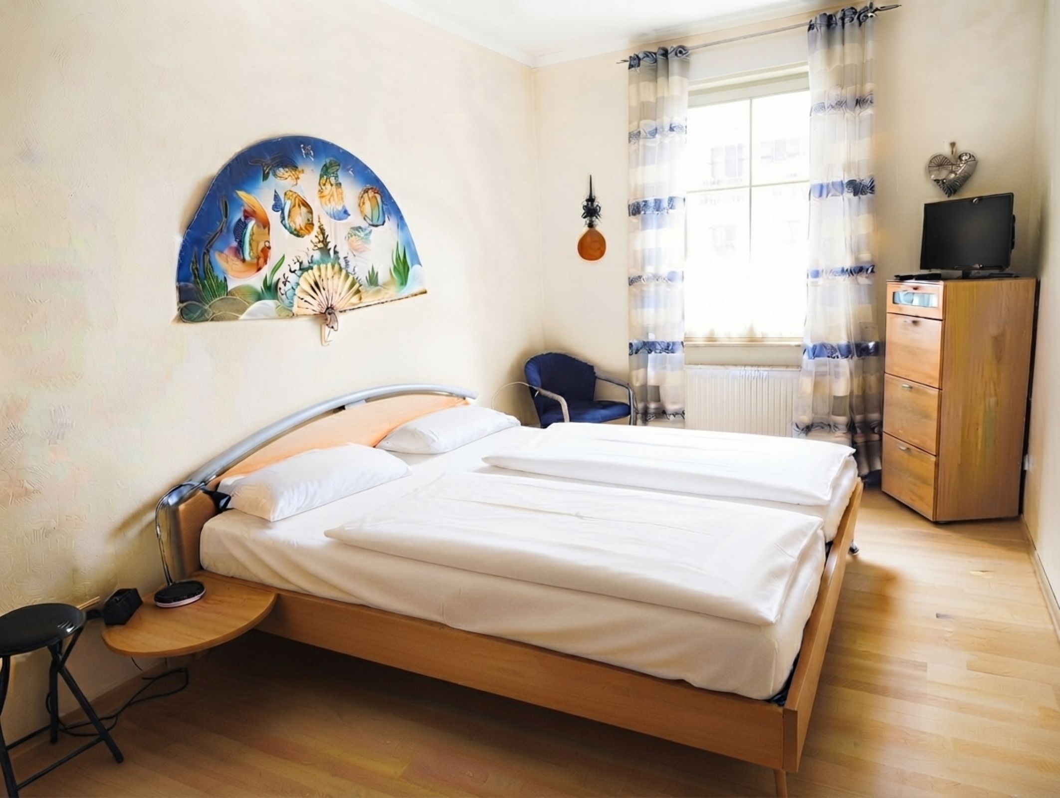 Een slaapkamer met een bed, een stoel, een bureau, een dressoir en een schilderij aan de muur.
