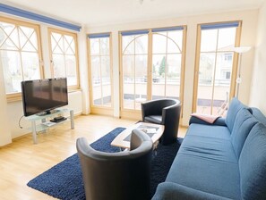 Uma sala de estar moderna com televisão de tela plana, um sofá, duas poltronas e uma mesa de centro.