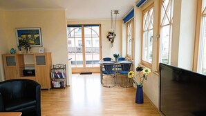 A living room with a TV, a dining table with chairs, a bookshelf, and a large window with a view of the outside. - Residence Starfish Ws.03 - Starfish Ws.03 (Kühlungsborn)