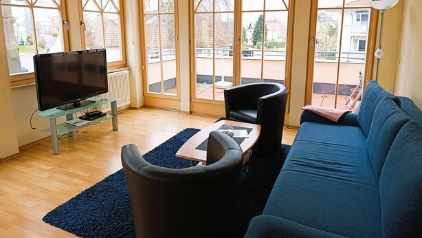 A living room with a blue sofa, a black armchair, a glass coffee table, and a TV on a stand. - Residence Starfish Ws.03 - Starfish Ws.03 (Kühlungsborn)