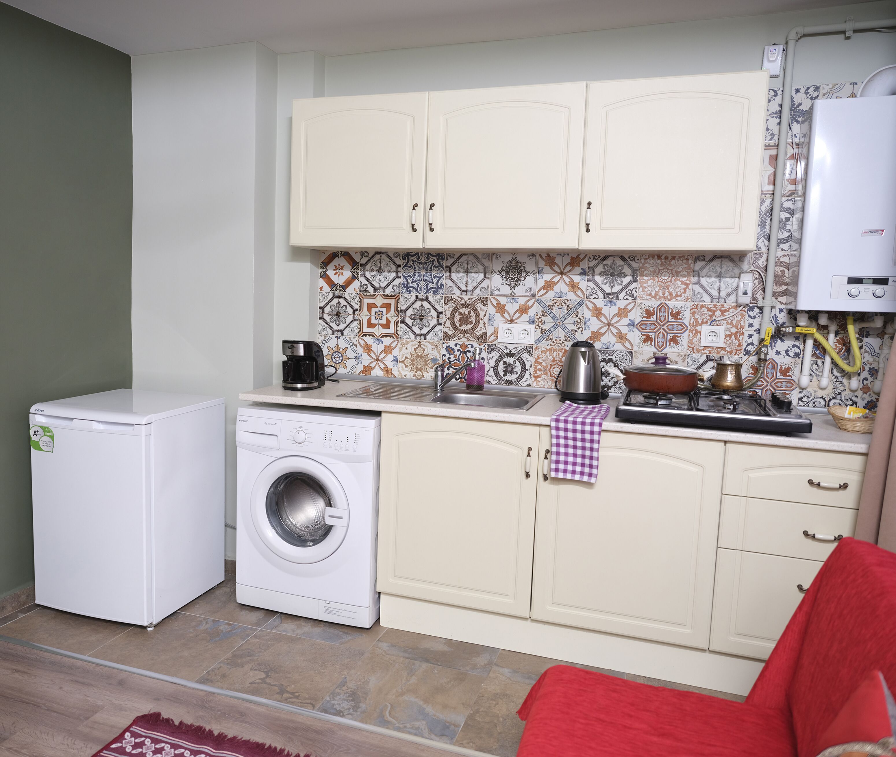 A compact kitchen with a washing machine, a coffee maker, and a kettle on the counter.