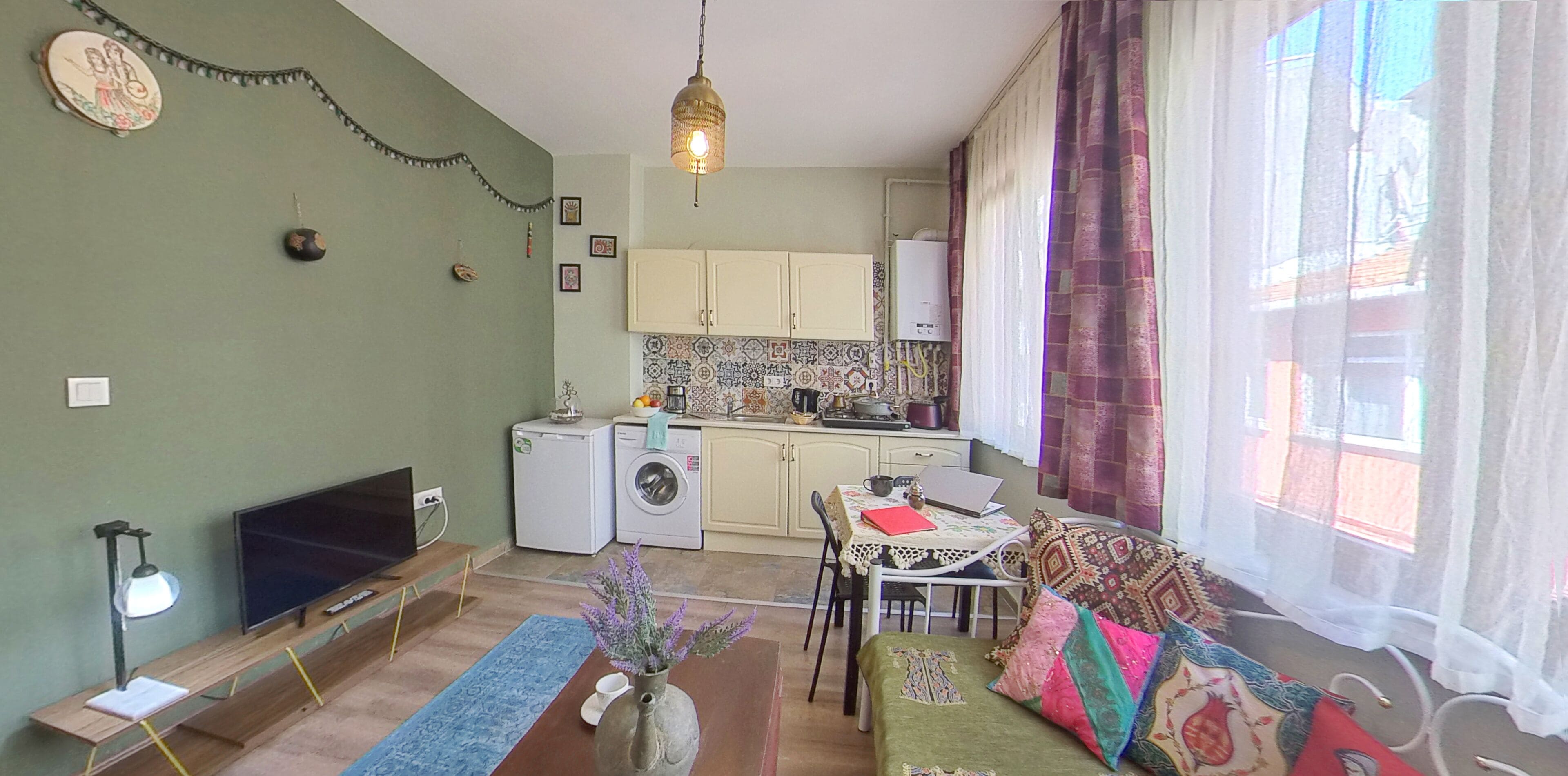 A compact living space with a TV, washing machine, kitchenette, dining area, and a bed.