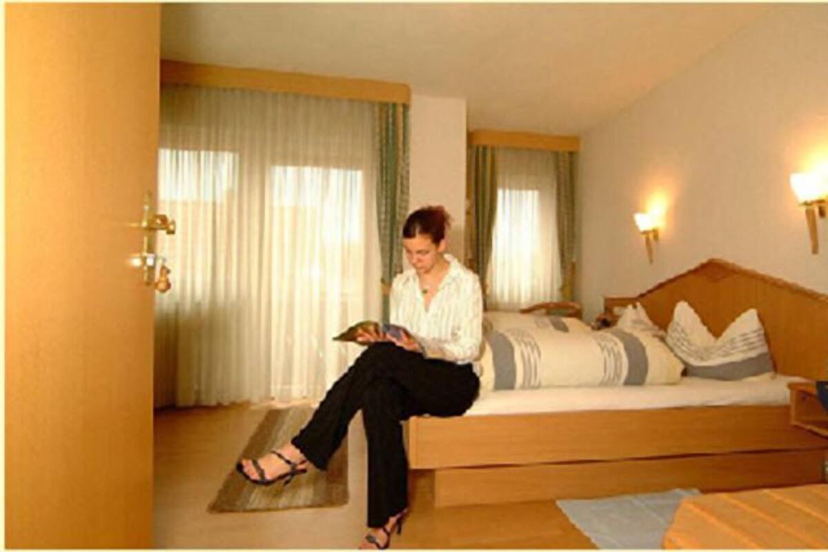 Una habitación con una cama, una lámpara de lectura y una ventana con cortinas.