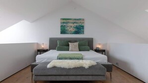 Ein Schlafzimmer mit Bett, Kissen, Nachttisch, Lampe und einem Bild an der Wand.