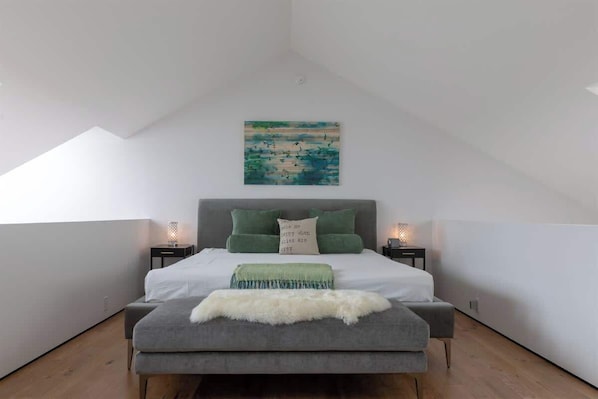 A bedroom with a bed, pillows, a bedside table, a lamp, and a painting on the wall.