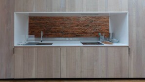 Eine Küche mit Ziegelrückwand, Holzschränken und einer weißen Arbeitsplatte.