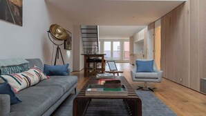 Ein modernes Wohnzimmer mit einer Couch, einem Couchtisch und einer Lampe. Eine Treppe führt in einen anderen Raum.