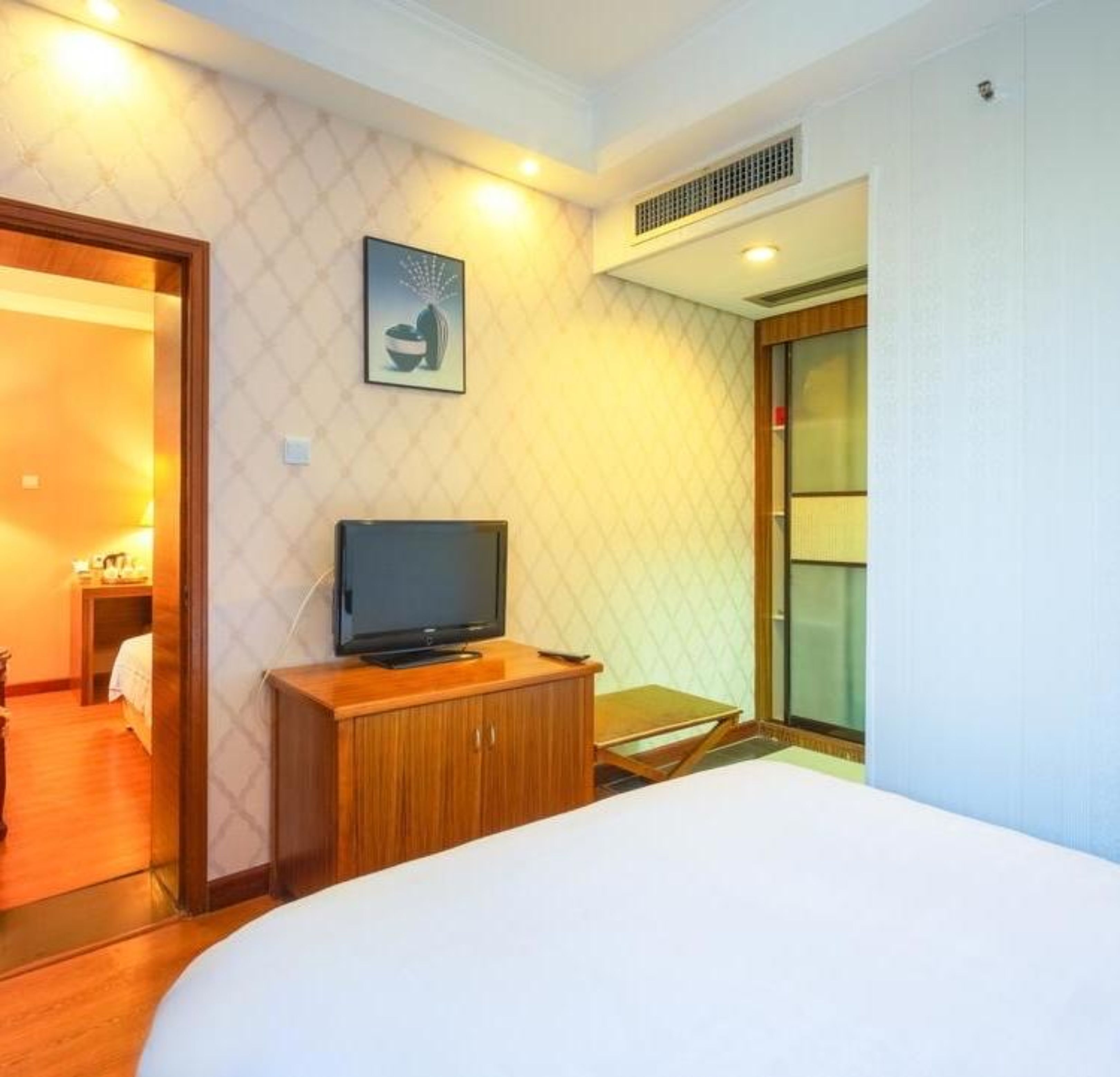 A hotel room with a bed, a television on a wooden cabinet, a picture on the wall, and a sliding door to the left.