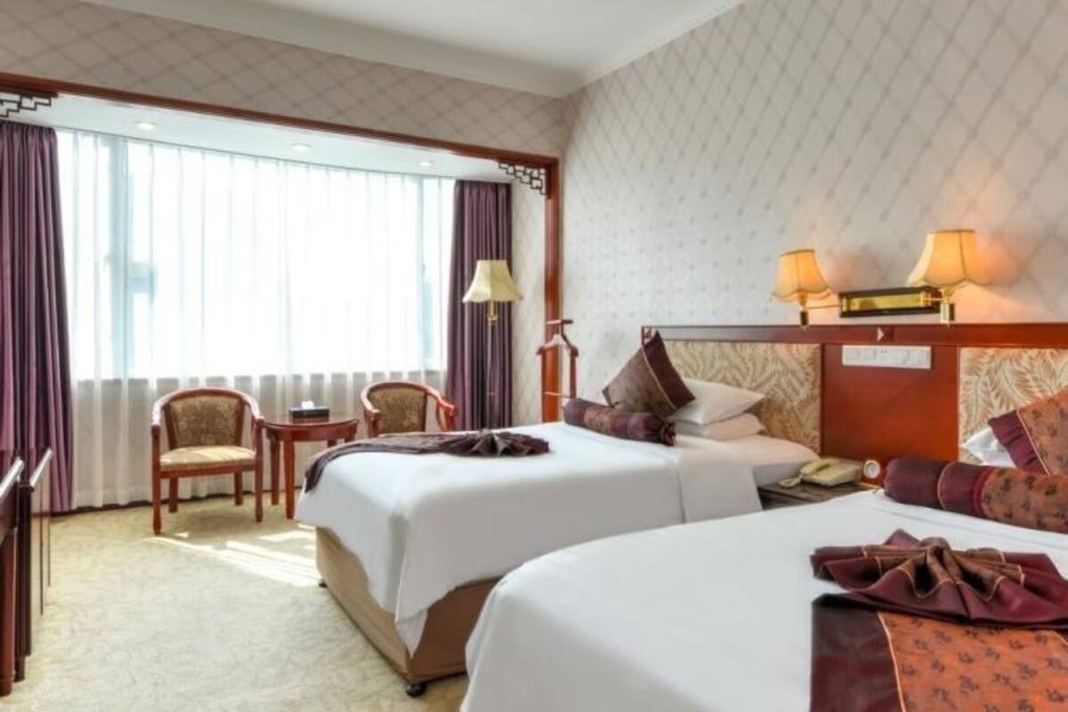 Habitación de hotel con dos camas, un escritorio, una silla y una ventana con cortinas.