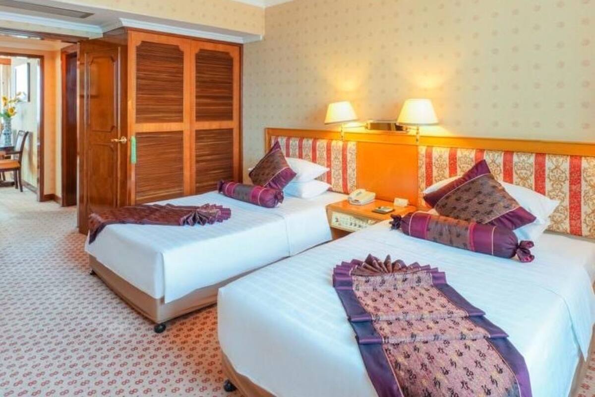 Habitación de hotel con dos camas, un armario de madera, un escritorio con lámpara y una pared con diseño.