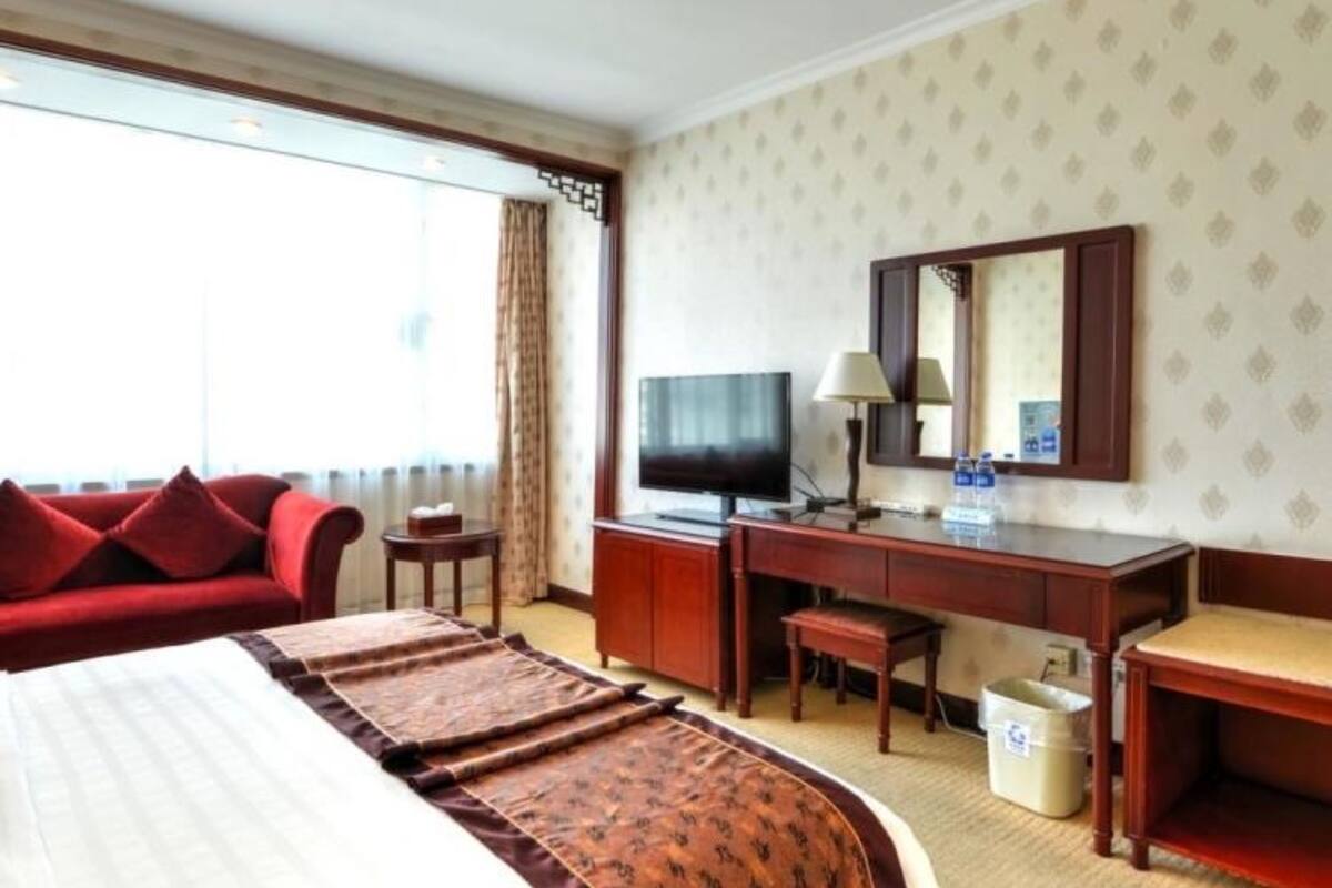 Habitación de hotel con una cama grande, un escritorio con televisor, una silla y una mesita.