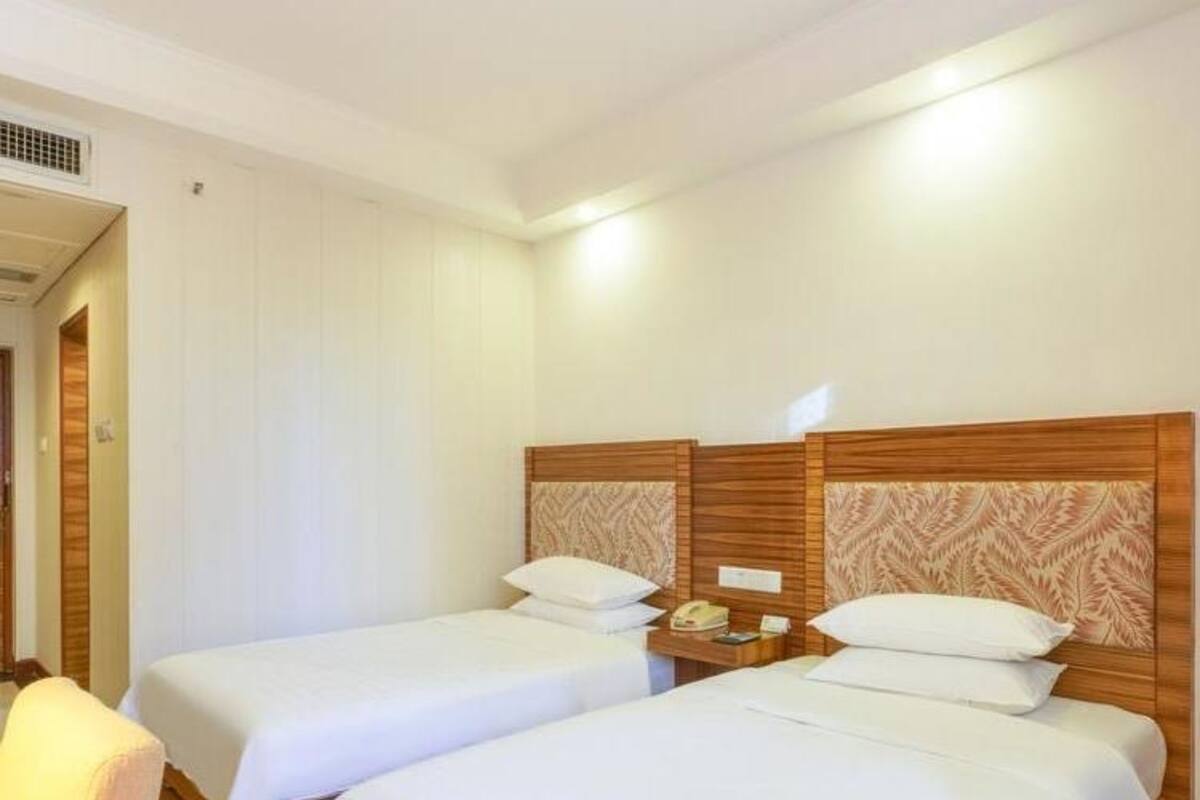Una habitación de hotel con dos camas individuales, cabecero de madera, mesita de noche con lámpara y una silla.