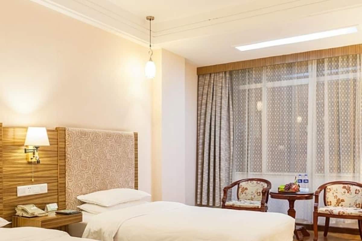 Habitación de hotel con dos camas, cabecero de madera, escritorio con lámpara y una silla.