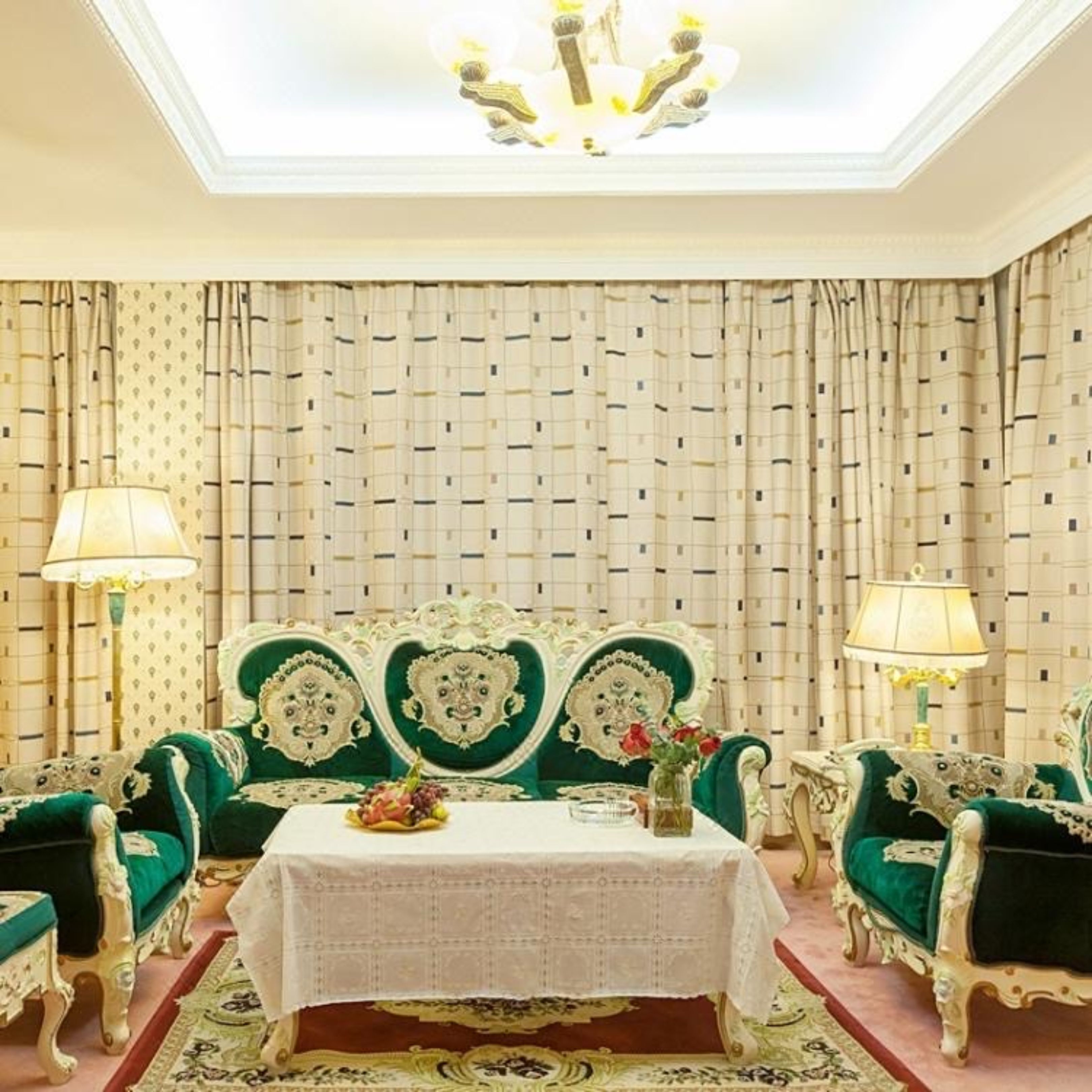 Una habitación con un sofá tapizado en verde, una mesa blanca con un centro de mesa floral y un telón de fondo con estampado.