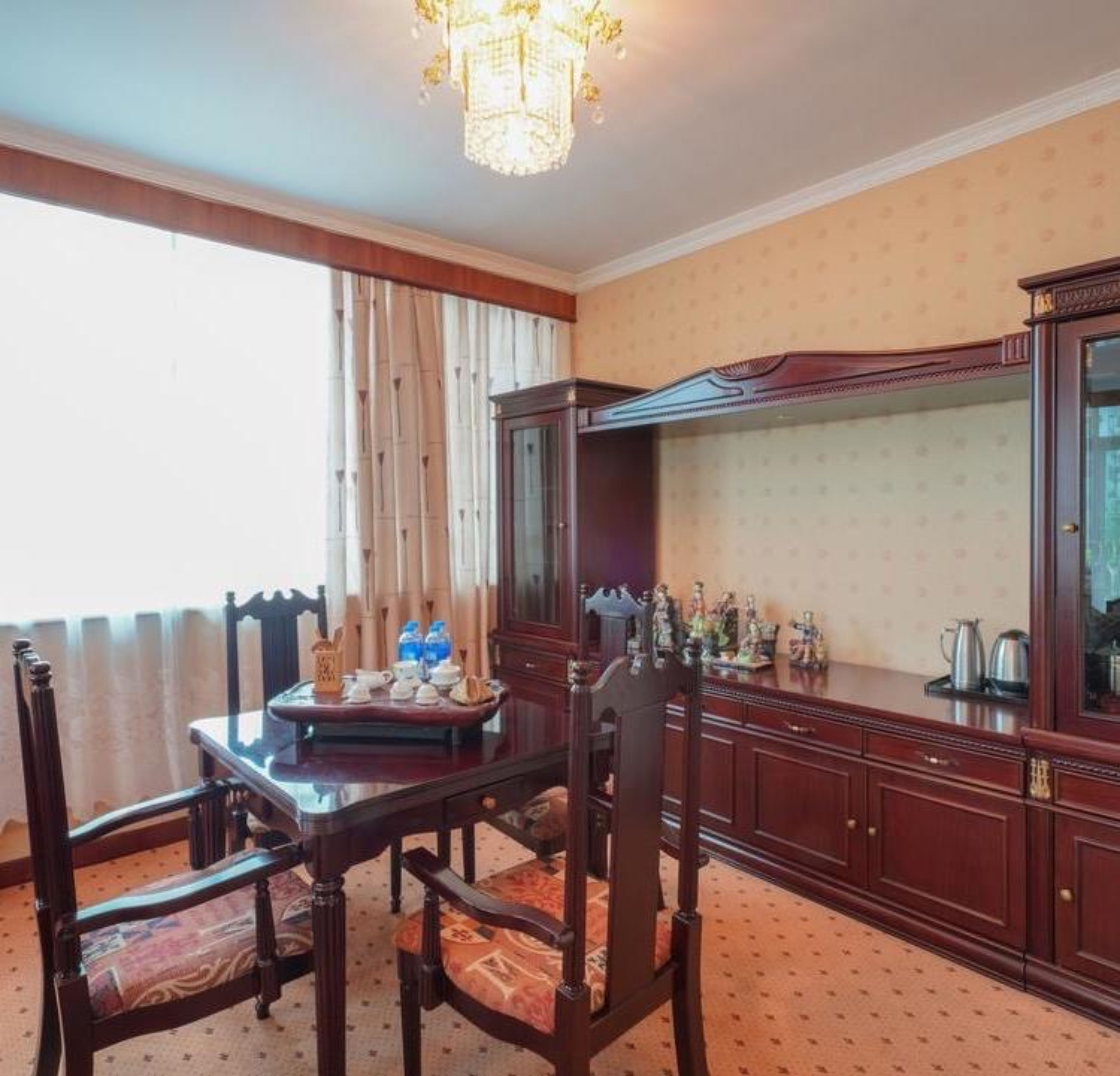 A room with a dining table set for four, a large wooden cabinet, and a chandelier.
