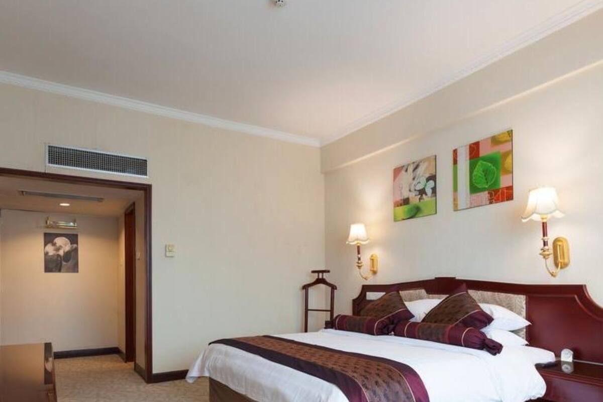 Habitación de hotel con una cama grande, un escritorio y una silla. Hay dos lámparas de pared y un cuadro en la pared.