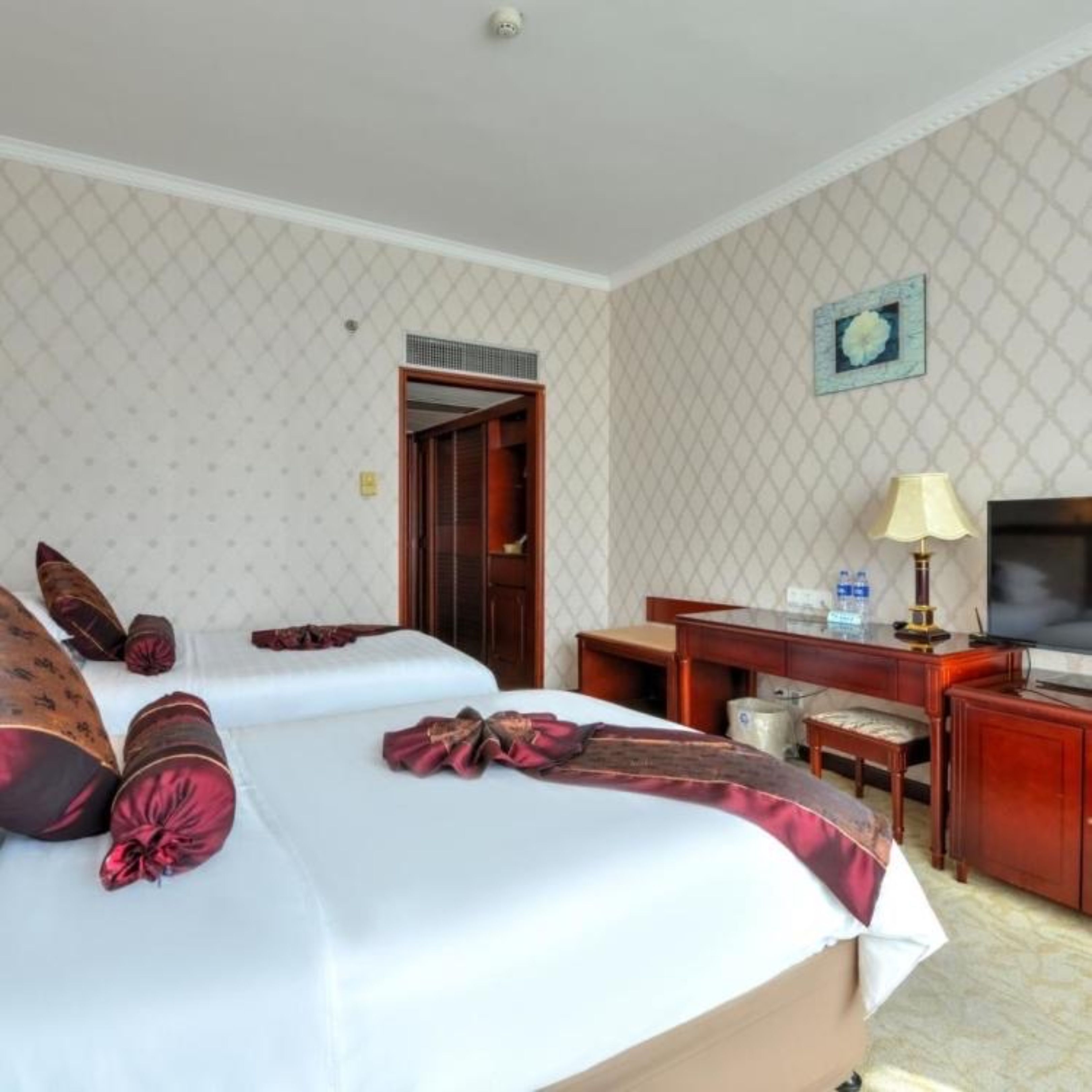 A hotel room with two beds, a desk with a chair, a television, and a small table with a lamp.
