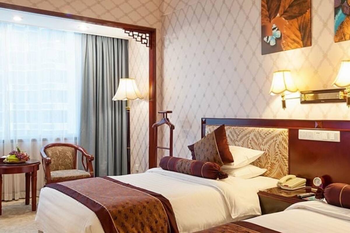 Habitación de hotel con dos camas, un escritorio, una silla y un amplio ventanal con cortinas.