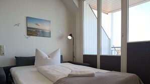 Ein Hotelzimmer mit einem Bett, einem Gemälde, einer Lampe und einem Fenster mit Jalousien.