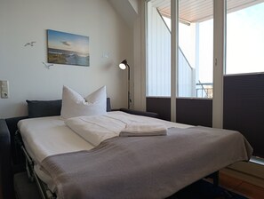A hotel room with a bed, a painting, a lamp, and a window with blinds.