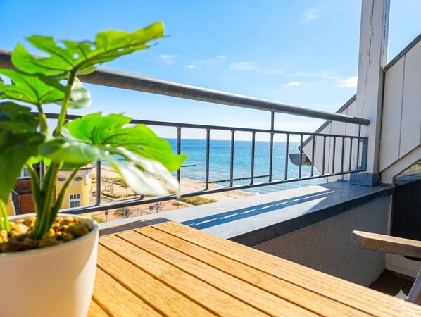 A balcony with a view of the sea, a potted plant, and a wooden table.
