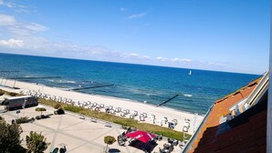 Blick auf den Strand mit einem geparkten Nordman-Lkw, Liegestühlen und einem Segelboot in der Ferne.