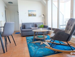 Ein modernes Wohnzimmer mit einer Couch, zwei Sesseln, einem kleinen Tisch und einer Zimmerpflanze.