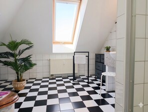 Ein modernes Badezimmer mit Schachbrettboden, einem Oberlicht, einem Heizkörper, einem Handtuchhalter, einem Waschbecken und einer Topfpflanze.