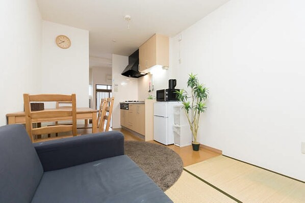 A compact living space with a sofa, dining table, and kitchen area including a microwave and refrigerator.