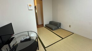 Una habitación con esteras de tatami, un sofá, una mesa de vidrio con un control remoto y un termostato fijado a la pared.