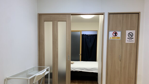 Habitación con cama, escritorio y armario. Se observan carteles que indican prohibido fumar y prohibido vapear.