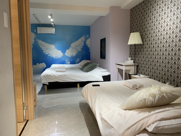 Two beds with white bedding and fluffy pillows, a desk and chair, and a mural of the sky adorn this stylish room.