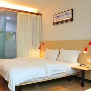 Una habitación de hotel con cama, mesita de noche, lámpara roja, un cuadro en la pared y ventana con cortinas.